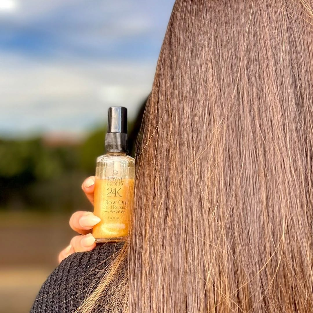 Person holding a bottle of 2K hair oil with a blurred outdoor background