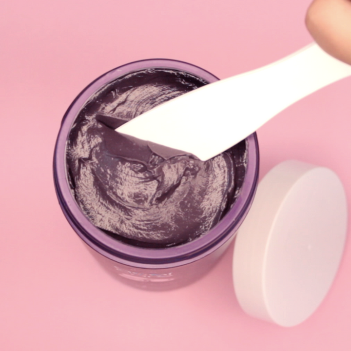 Jar of black cream with a spatula on a pink background